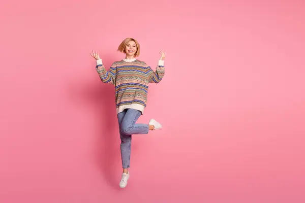 ポジティブなゴージャスな少女のフルサイズの写真は ピンク色の背景で孤立した手を上げて飛ぶ装飾セータージーンズズズを着用します — ストック写真