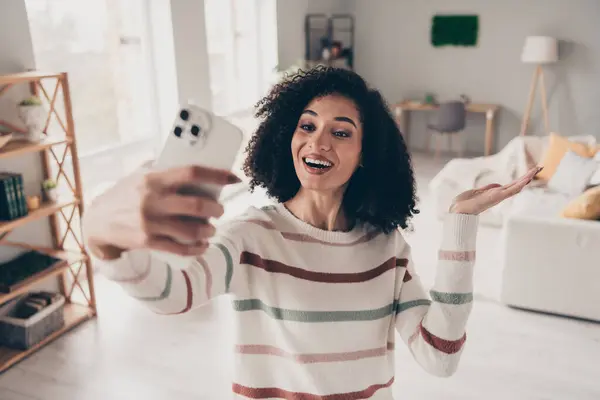 Photo of excited funky lady dressed striped pullover tacking selfie modern gadget indoors apartment room.