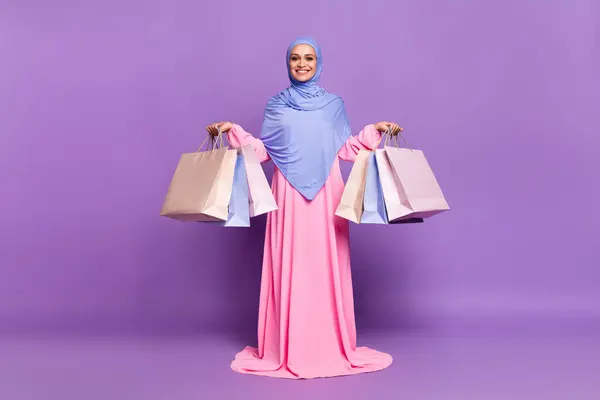 ファンキーな若い女性のフルサイズの写真は バイオレット色の背景に隔離されたブルーヒジャブイスラム教のピンクのドレスを着用バッグを保持しています — ストック写真