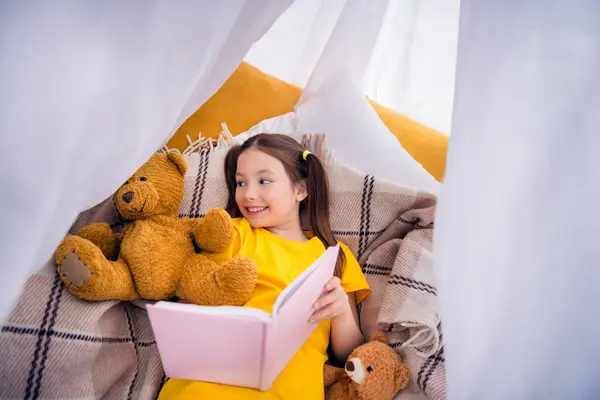 图片肖像可爱的小女孩躺在地板帐篷里看书玩具穿着时髦的黄色衣服幼儿园的内部 — 图库照片