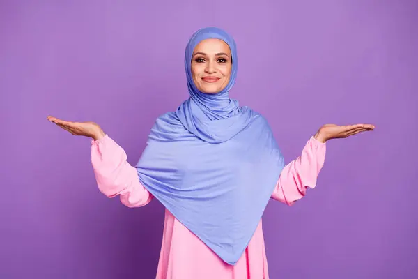 楽観的な若い女性の写真は 紫色の背景の上に隔離された青いピンクのアラブの民族衣装を着て空のスペースを保持しています — ストック写真