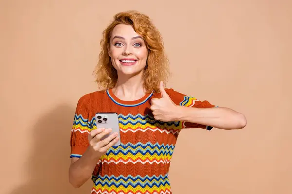 穿着T恤衫的女孩满意的照片拿着智能手机 展示她的大拇指 在苍白的背景下表现得很好 — 图库照片
