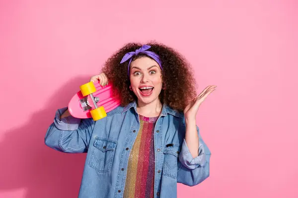 Photo of cheerful excited lady dressed denim outfit rising arm holding penny board empty space isolated pink color background.