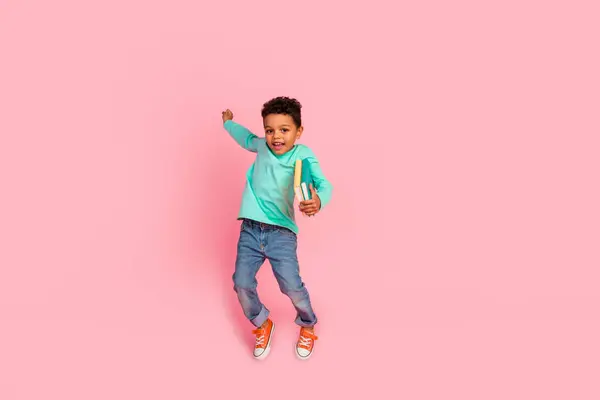 可爱小男孩跳过书架的全身照片 穿着时髦的淡蓝色衣服 背景是粉色的 很有意思 — 图库照片
