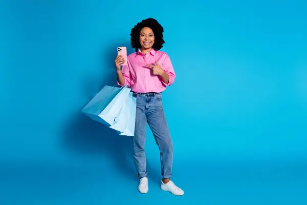 かなり若い女性ポイントのフルサイズの写真 指のスマートな携帯電話は青い色の背景で隔離されたピンクのシャツを着ます — ストック写真