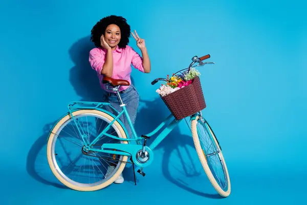 良い気分快適な女の子の完全な長さの写真 シルクシャツジーンズは ブルーカラーの背景に隔離されたVシンボルを示す自転車に傾いています — ストック写真