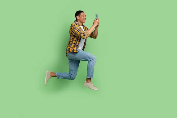 用绿色背景隔离的智能电话跳跃式空格来描绘运动健将的全长肖像 — 图库照片