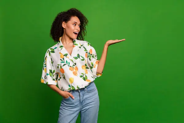 Photo of adorable impressed woman dressed print shirt showing arm looking empty space isolated green color background.