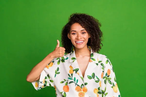 Photo of positive confident woman dressed print shirt smiling showing thumb up isolated green color background.