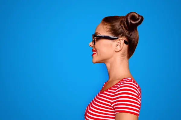Half-faced side profile view portrait of happy confident woman dressed in striped shirt and spectacles isolated on red background with copy space for text.