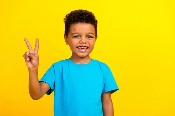 穿着蓝色T恤衫 头戴鲜艳黄色背景的V字形标志的快乐而积极的学童的画像 — 图库照片