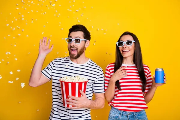 Portrait of two impressed people hold soda can throw pop corn watch movie 3d glasses isolated on yellow color background.