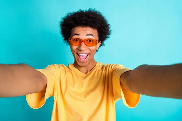 Photo of overjoyed funky guy with afro hair dressed yellow t-shirt in sunglass making selfie isolated on turquoise color background.
