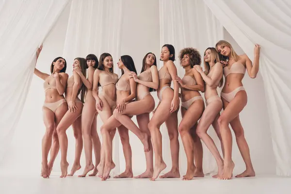 No retouch full length photo of diverse women in underwear standing together isolated over light background.
