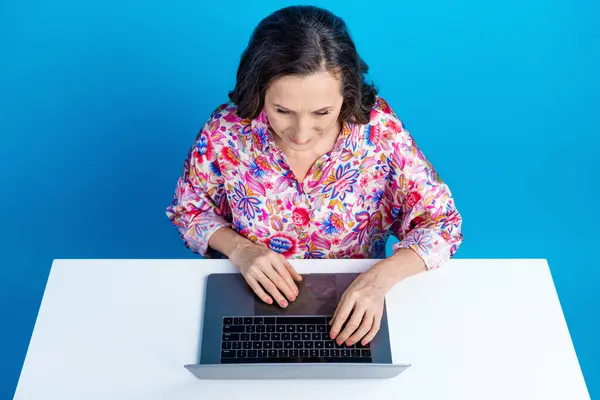 有魅力的老年女性的照片肖像坐在桌面上上网本穿着时尚艳丽的衣服 背景为蓝色 — 图库照片