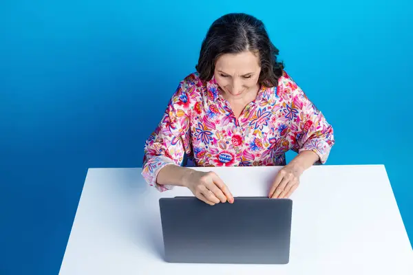 有魅力的老年女性的照片肖像坐在桌面上上网本穿着时尚艳丽的衣服 背景为蓝色 — 图库照片