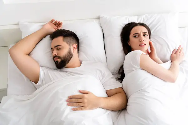 Photo of two people couple sleeping girl irritated with guy snoring in house.