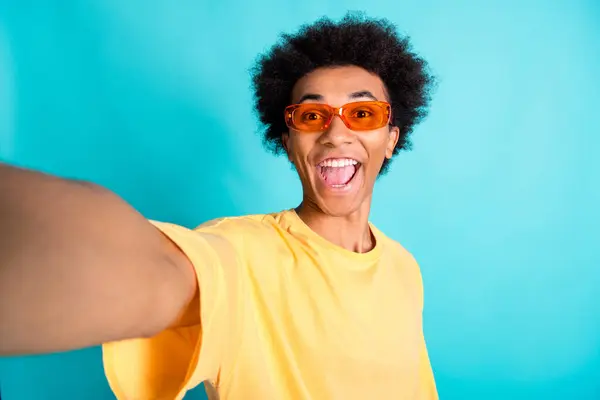 Portrait of overjoyed man with afro hairstyle wear oversize t-shirt in sunglass make selfie scream yes isolated on teal color background.
