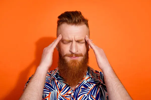 Photo of tired upset guy dressed print shirt smiling hands head feeling headache isolated orange color background.