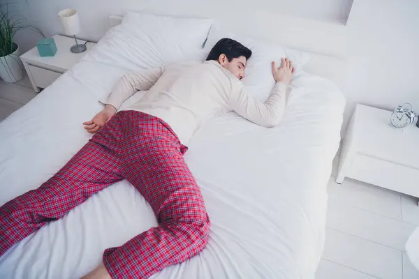 Photo of young attractive man sleeping lying alone in soft comfy bed white room interior indoors.