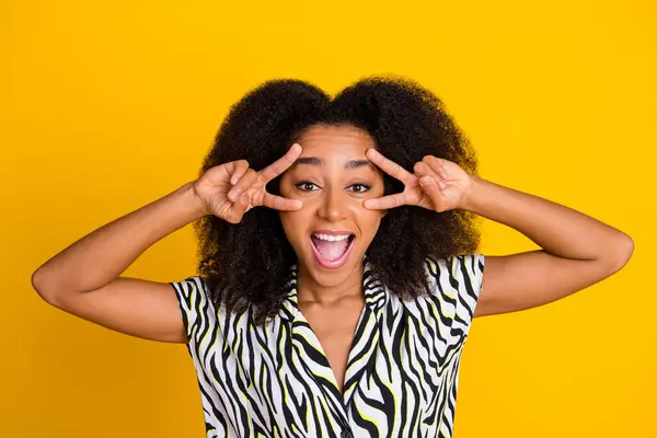 Portrait of young optimistic young girl with curly hair in zebra print shirt showing double v sign face isolated on yellow color background.