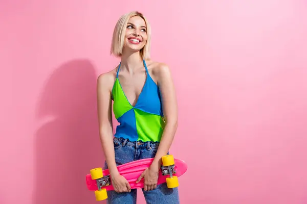 Portrait of friendly woman with bob hair wear colorful top hold skateboard look at promo empty space isolated on pink color background.