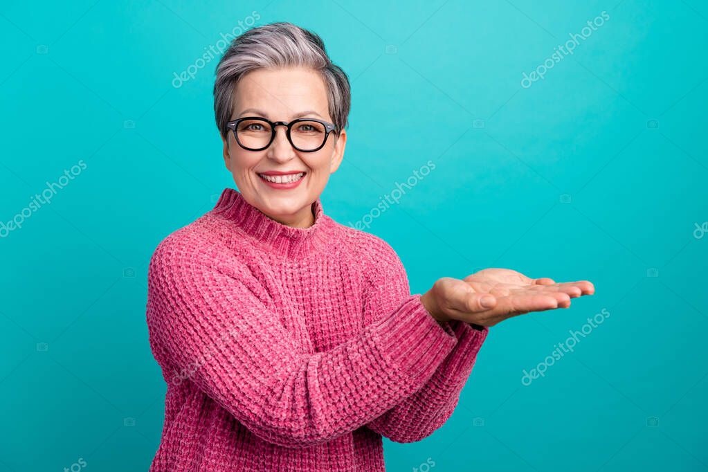 Portrait of toothy beaming woman wear pink pullover in glasses palms presenting object empty space isolated on turquoise color background.