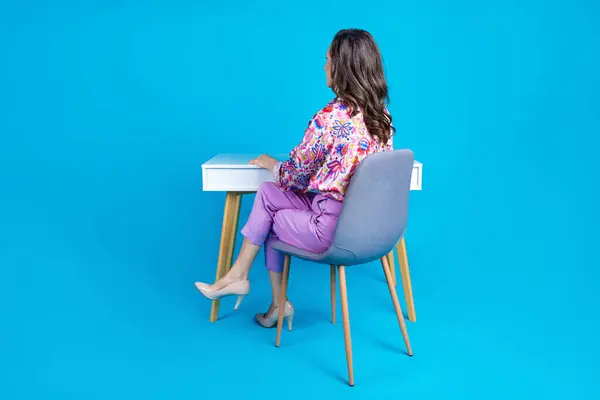 魅力的なシニア女性のフルサイズの写真は 青色の背景に隔離されたスタイリッシュなカラフルな服の背後にあるテーブルに座ります — ストック写真