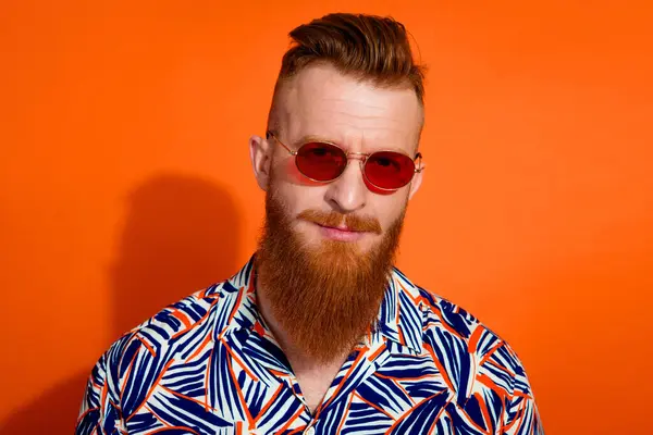 Photo of virile guy with red beard trendy haircut wear stylish shirt in sunglass look at you isolated on vibrant orange color background.
