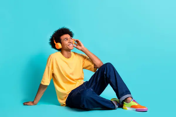 Full size photo of satisfied man wear oversize t-shirt listen music in headphones look empty space isolated on teal color background.