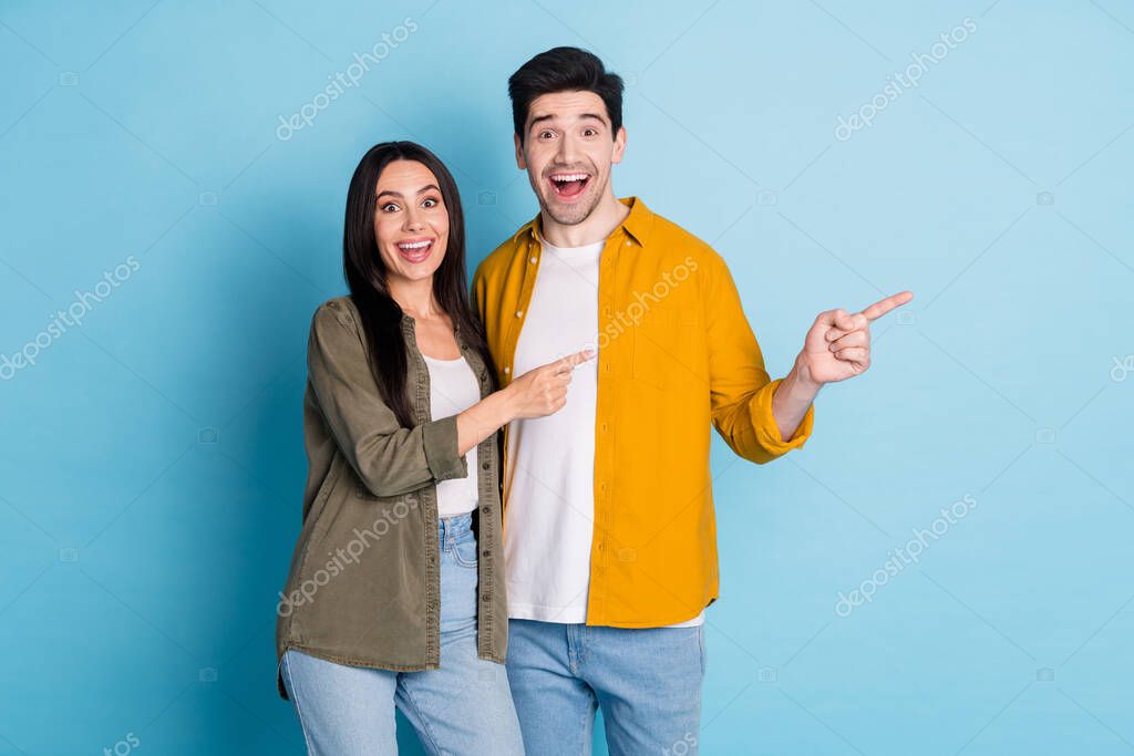 Portrait of two young people indicate fingers empty space wear shirt isolated on blue color background.