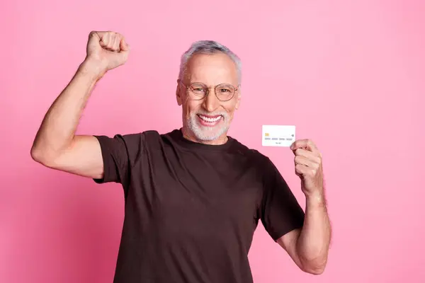 stock image Portrait of positive senior man with beard dressed t-shirt in glasses holding credit card win lottery isolated on pink color background.