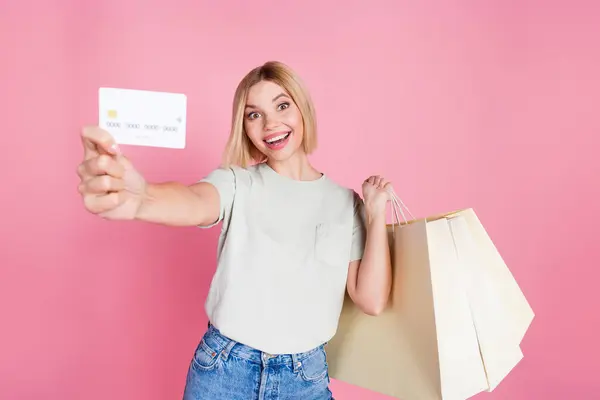 Stock image Photo of impressed woman with bob hairstyle dressed t-shirt holding shopping bags show you debit card isolated on pink color background.