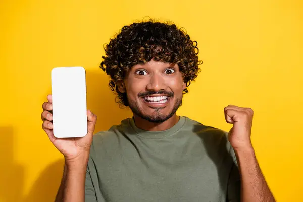 stock image Photo of satisfied guy dressed t-shirt demonstrate smartphone touchscreen empty space win lottery isolated on yellow color background.