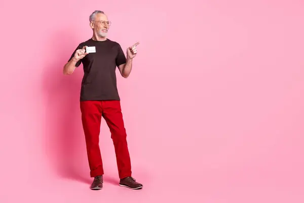 stock image Full size photo of smart man dressed t-shirt in glasses indicating look empty space hold credit card isolated on pink color background.