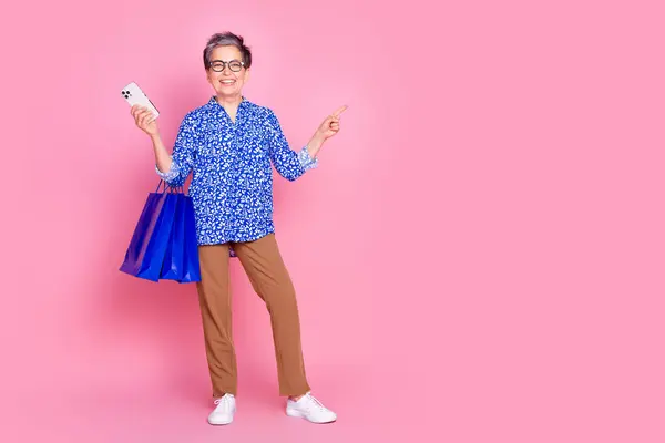 Stock image Full size photo of satisfied person dressed blouse hold shopping bags smartphone indicating empty space isolated on pink color background.