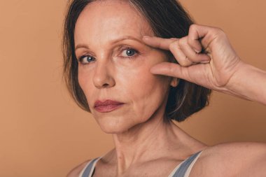 No retouch close up photo of charming elderly woman face lifting isolated on beige color background. clipart