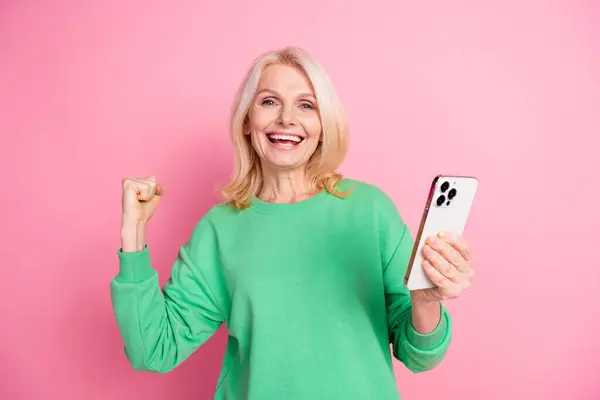 Stock image Photo portrait of lovely senior lady hold device winning dressed stylish green garment isolated on pink color background.