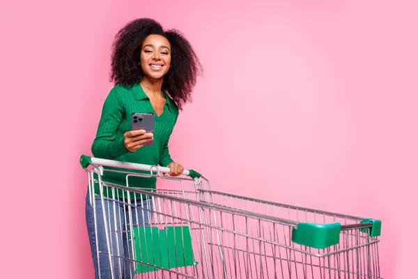 stock image Photo portrait of attractive young woman push supermarket cart hold device dressed stylish green clothes isolated on pink color background.