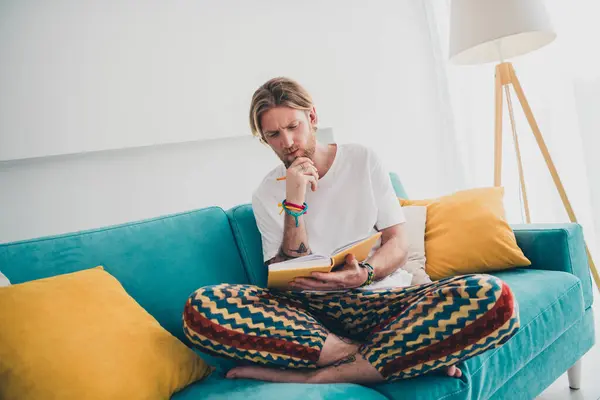 stock image Full size photo of nice young man sit couch read book thoughtful wear stylish pajama modern light cozy interior flat indoors.