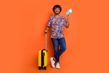 Full length photo of handsome young man baggage hold tickets dressed stylish colorful garment isolated on orange color background. clipart