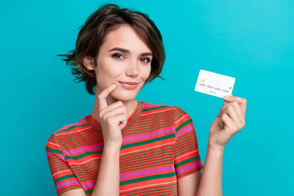 stock image Portrait of minded girl with short hairdo wear stylish t-shirt demonstrate credit card finger on cheek isolated on teal color background.