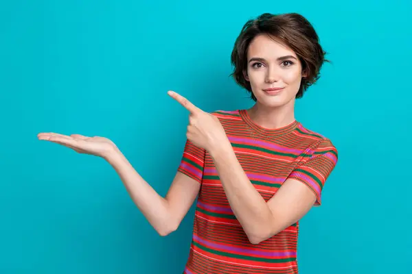 stock image Portrait of cheerful girl with short hair wear stylish t-shirt indicating at product on arm empty space isolated on teal color background.