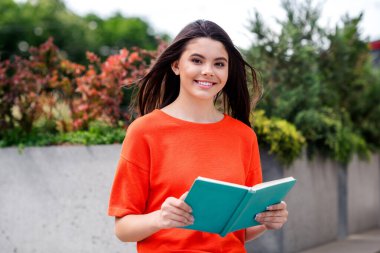 Photo of attractive teen cheerful girl read book relax wear red garment having fun outside outdoors. clipart