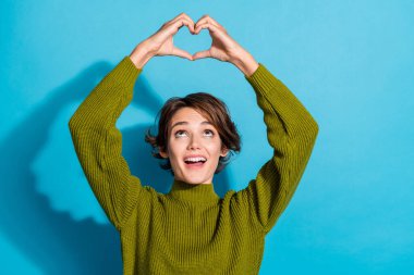 Photo of adorable lovely cute girl wear khaki clothes two arms above head heart figure love compliment isolated on cyan color background. clipart