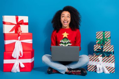 Full length photo of young lady pile gifts netbook look up empty space excited christmas garment celebrate holidays on blue background. clipart