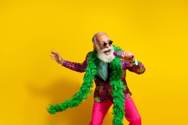 Photo of crazy grandfather sing microphone green scarf wear colorful clothes isolated on yellow background. clipart