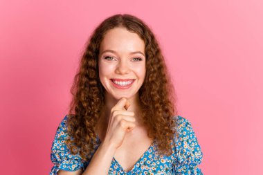 A cheerful young woman with curly hair smiles confidently while posing in a blue floral dress. The vibrant pink background enhances her joyful expression. clipart