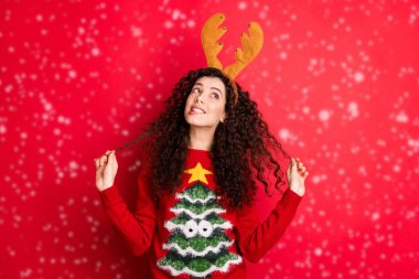 Photo of funny curly lady dreaming x-mas would bring peace and love to all people on earth looking empty space wear head horns pullover isolated red color background clipart