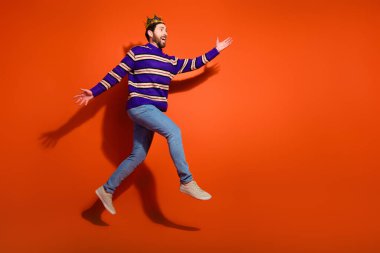 Full length photo of handsome young guy running excited fast dressed stylish striped purple garment isolated on orange color background. clipart